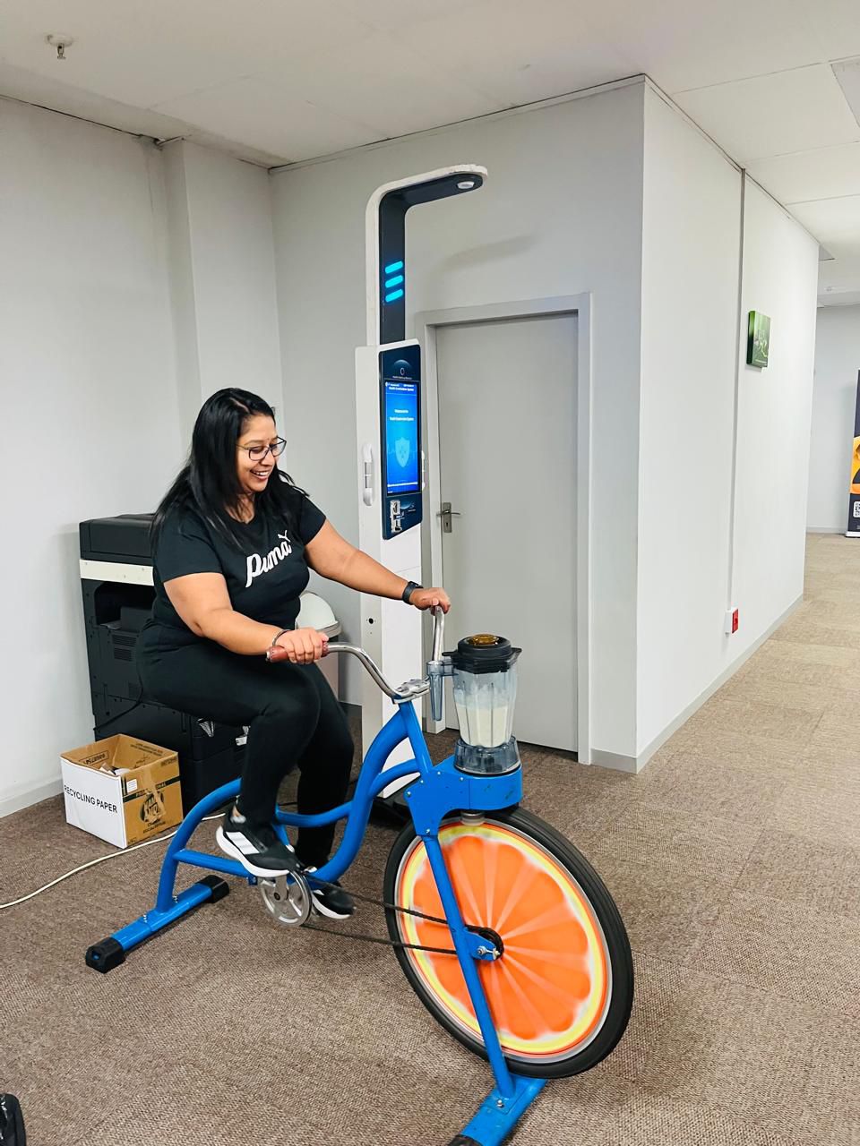 Rider pedalling a blue smoothie bike with an orange-slice wheel at an event